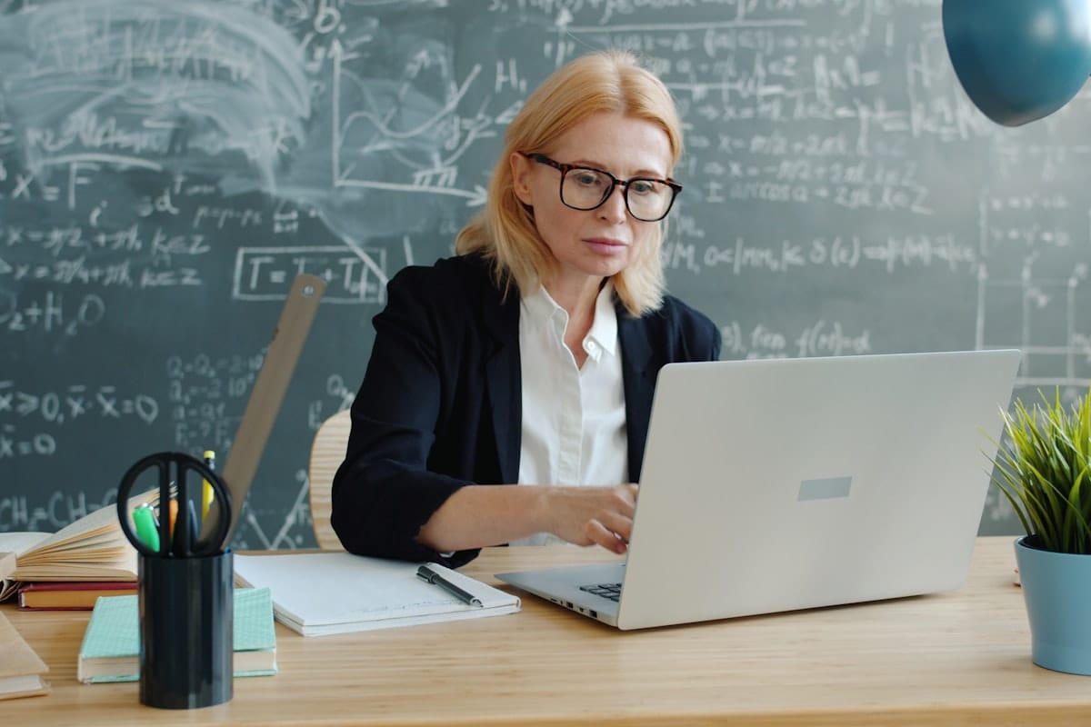 Enseignante travaillant sur un ordinateur portable devant un tableau noir